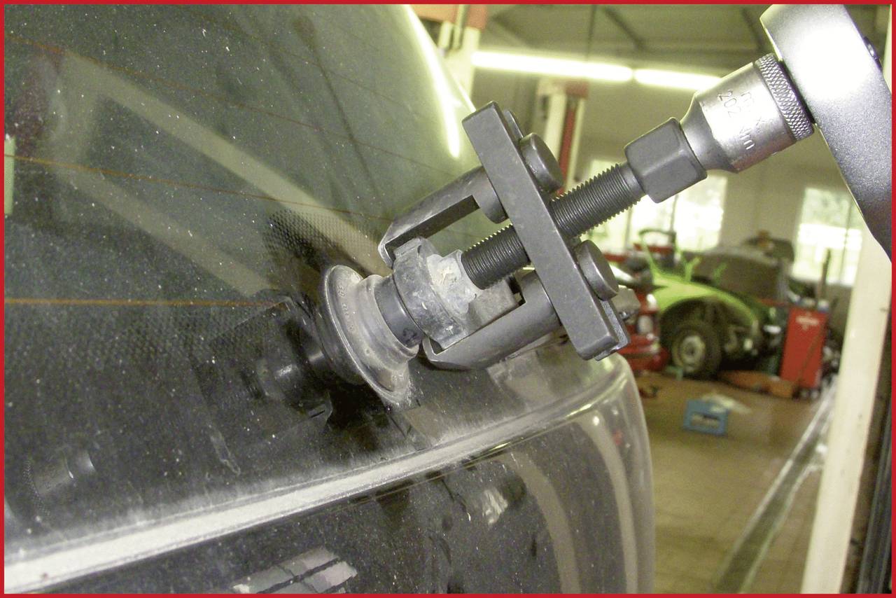 Reparatur eines Autofensters in einer Werkstatt. Ein Werkzeug ist an der Scheibe befestigt, um Schäden zu beheben. Im Hintergrund sind unscharfe Werkstattdetails erkennbar.
