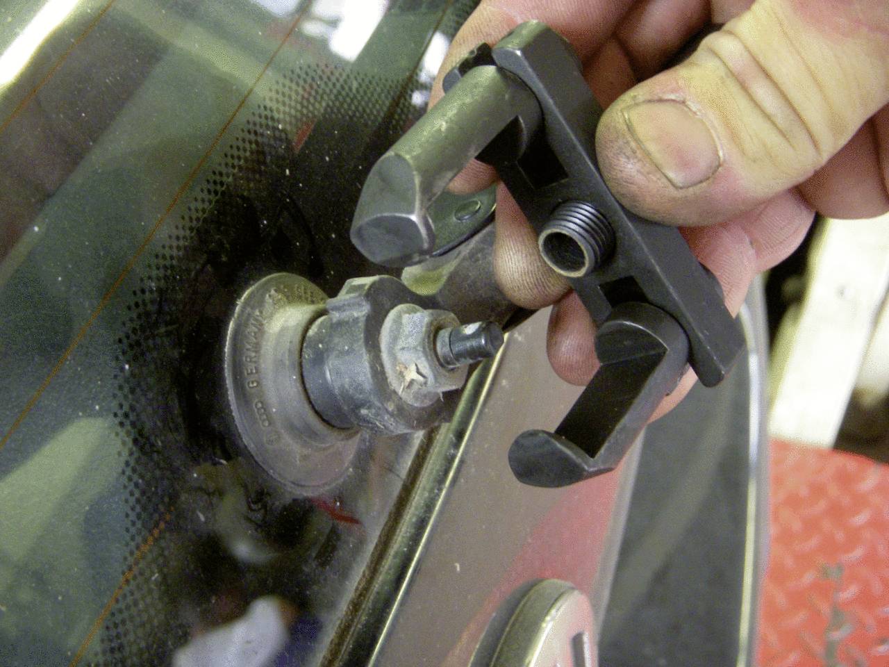 Eine Hand hält ein Werkzeug, das zum Entfernen eines Wischerarms von einem Autofenstermechanismus verwendet wird.