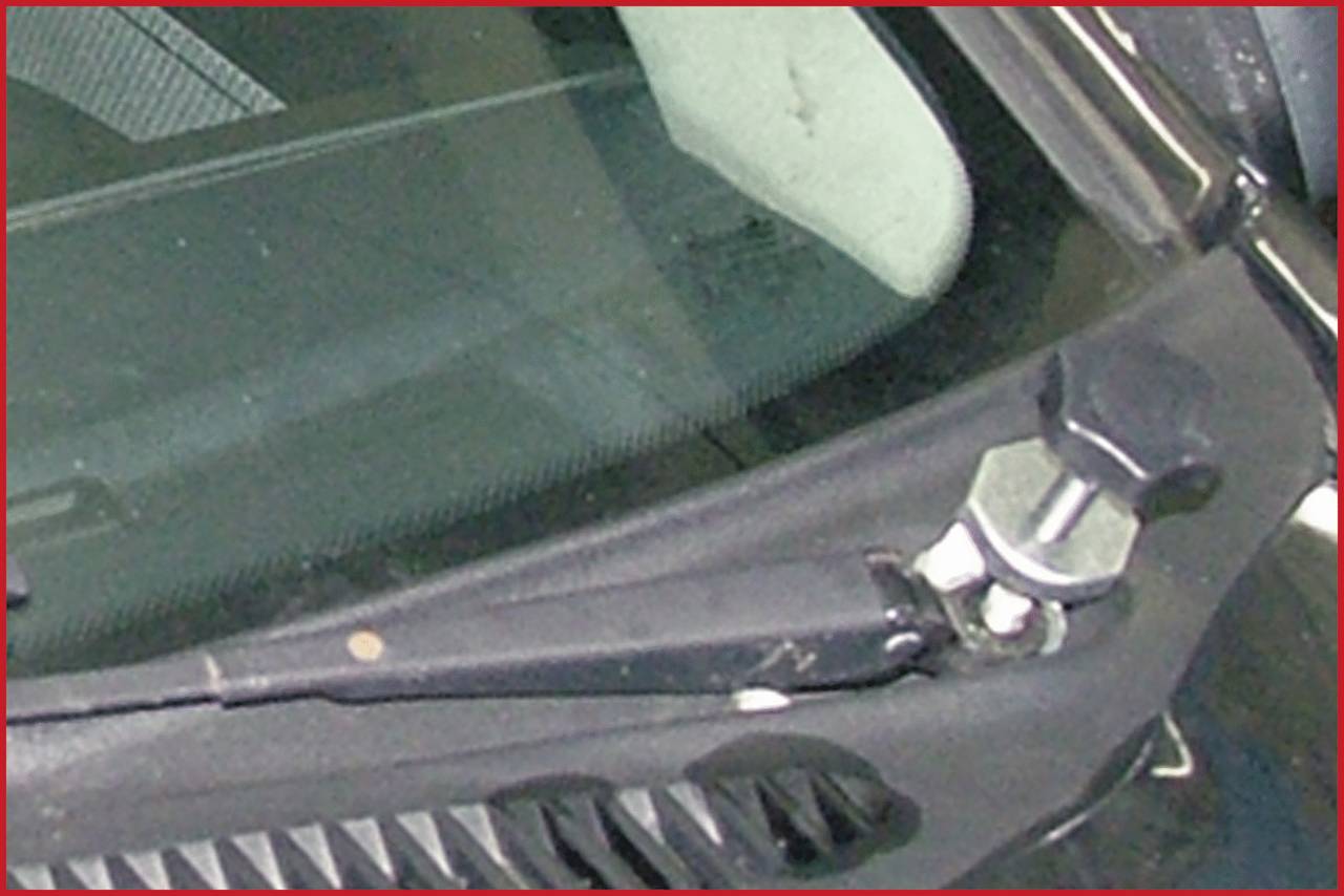 Nahaufnahme eines Scheibenwischers auf einer Autoscheibe. Der Wischerarm ist mit einer großen Schraube befestigt.
