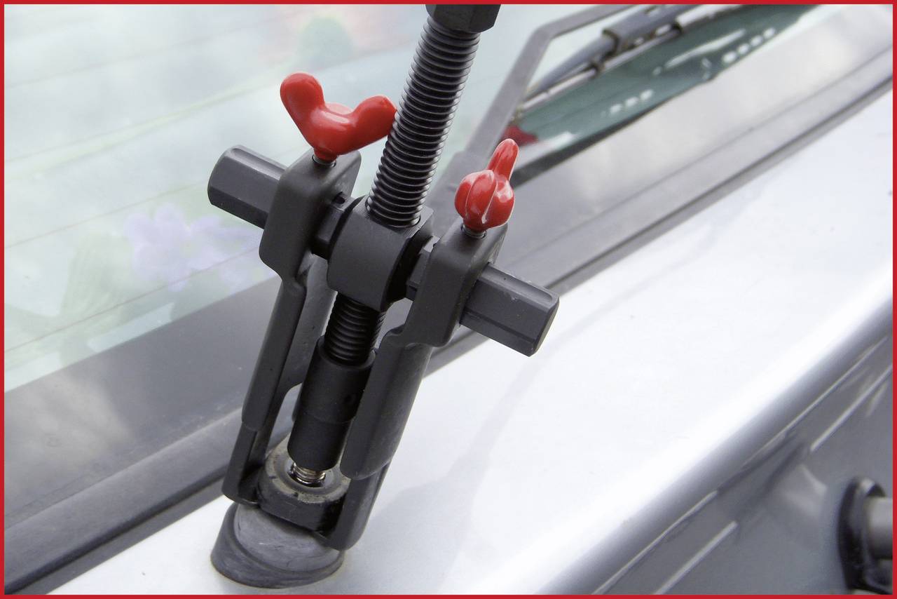 Ein Werkzeug zieht einen Scheibenwischerarm von einem Autowindschutzscheibenmotor ab. Der Hintergrund zeigt einen Teil des Autos.