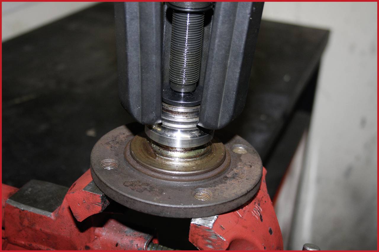 Nahaufnahme einer mechanischen Vorrichtung, die ein Lager an einer Metallplatte befestigt. Eine Werkbank im Hintergrund.