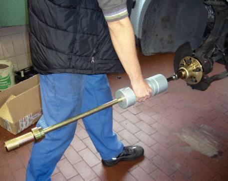 Eine Person verwendet ein spezielles Werkzeug, um ein Autoteil an einem Fahrzeug zu reparieren. Der Fokus liegt auf dem Werkzeug und der Anwendung.