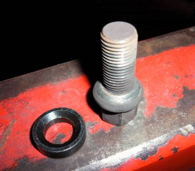 Ein Schraubbolzen und eine Unterlegscheibe liegen auf einer rotbraunen Metalloberfläche.