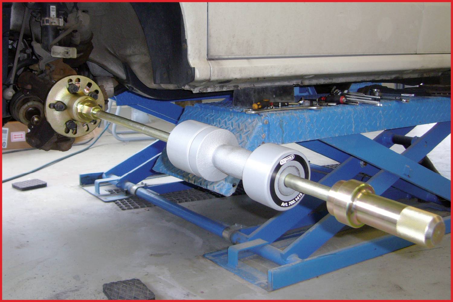 Ein Auto steht auf einer Hebebühne, ein Werkzeug installiert offenbar eine Mechanik am Rad der Vorderachse. Arbeitsaustauschumgebung.