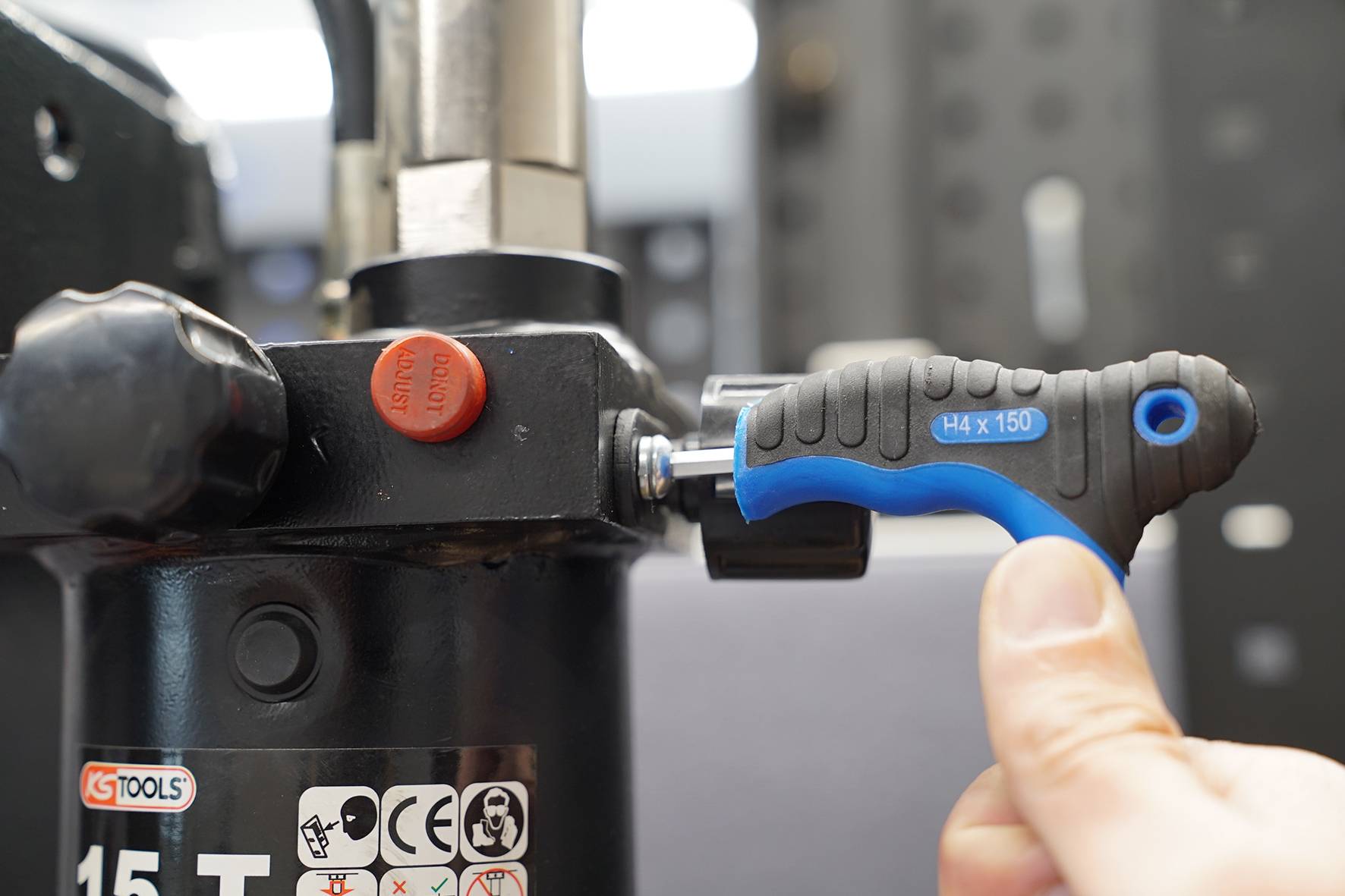 Eine Hand benutzt einen blauen und schwarzen Schraubendreher, um an einem mechanischen Gerät zu arbeiten.