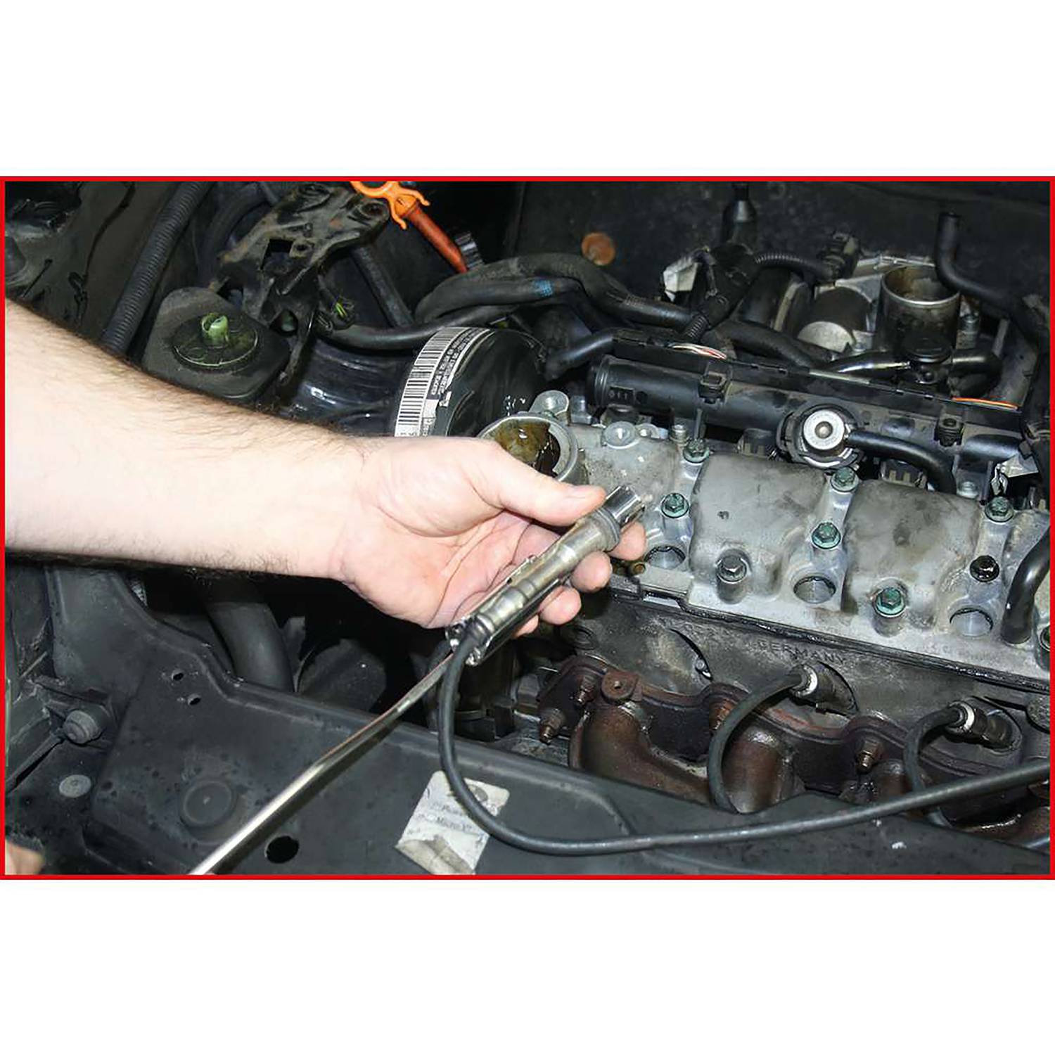 Eine Person hält eine Lambdasonde in der Hand vor einem Motorblock. Die Sonde ist für die Abgasmessung im Auto wichtig.