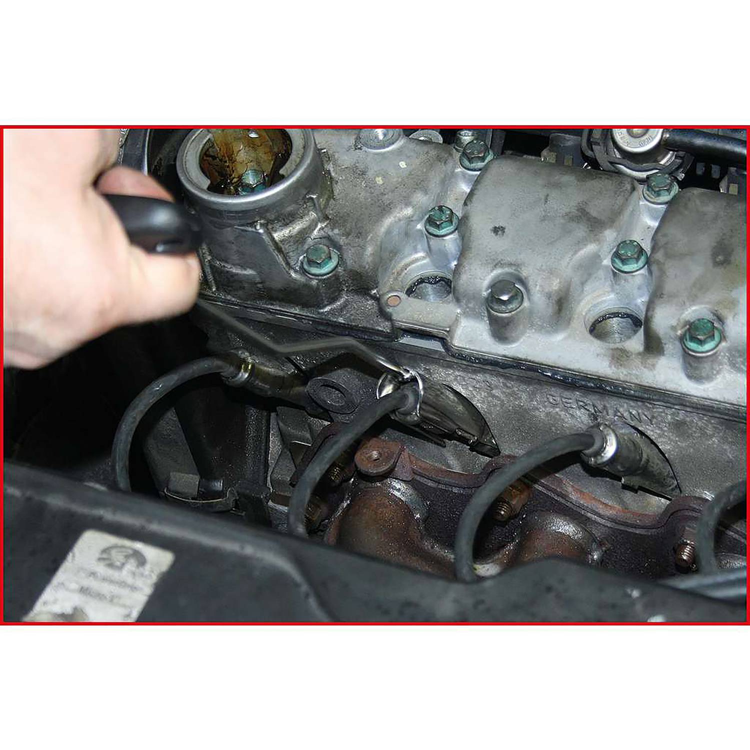 Ein Mechaniker zieht einen Zündkerzenstecker aus einem Zylinderkopf eines Autos. Man sieht Spuren von Verschleiß und Öl im Motor.