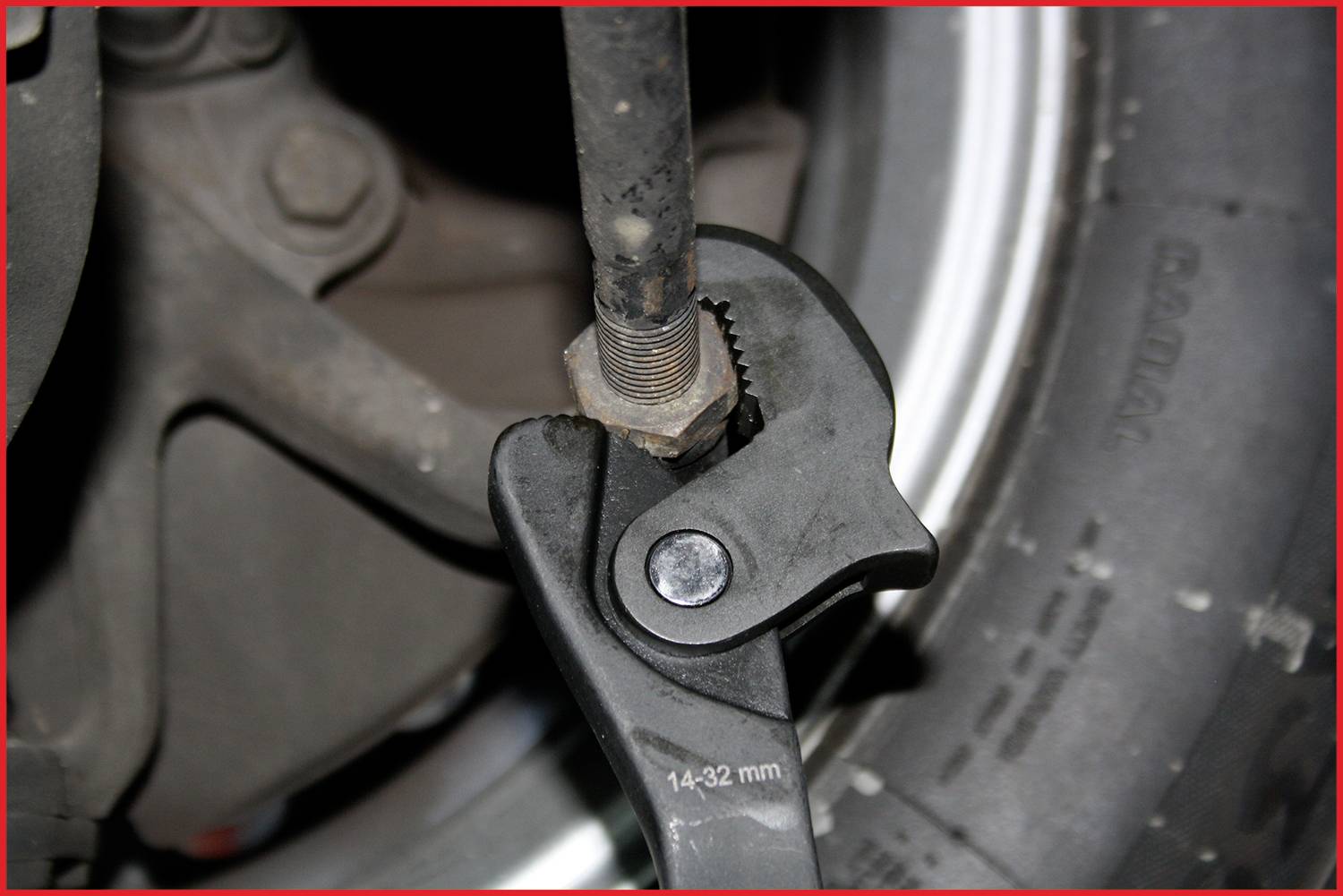 Ein Schraubenschlüssel zieht eine Mutter an einer Stange fest, die vor einem Reifen und einem Autoteil positioniert ist.