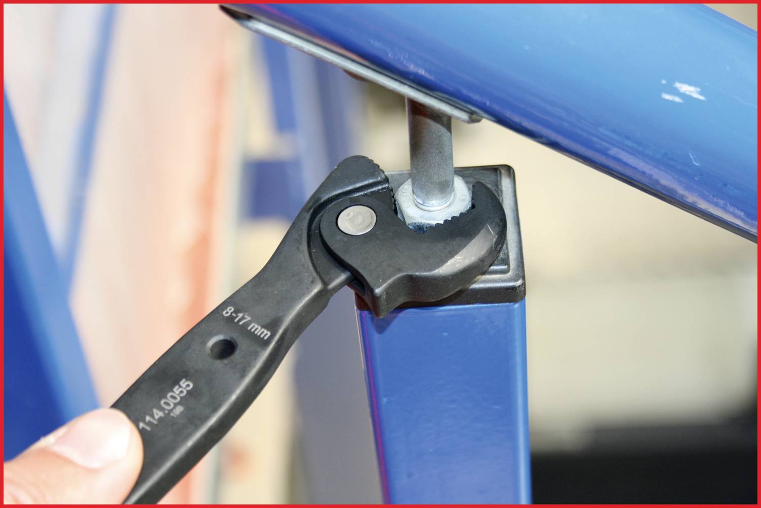 Eine Hand hält einen Schraubenschlüssel, der eine Mutter an einer blauen Metallstruktur festzieht.