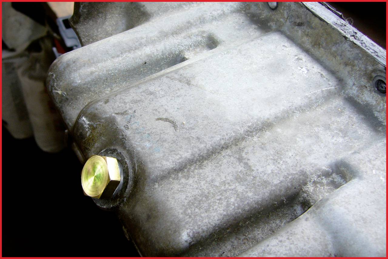 Nahaufnahme einer Metalloberfläche mit einem goldenen Sechskantschraubenkopf. Möglicherweise Teil eines mechanischen Geräts oder Motors.