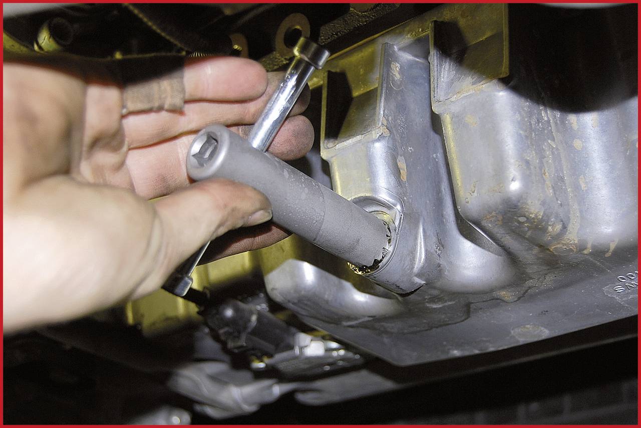 Ein Mechanikerhand benutzt ein Werkzeug, um eine Schraube an einer Metalloberfläche zu lösen, vermutlich an einem Fahrzeugmotor oder einer Maschine.