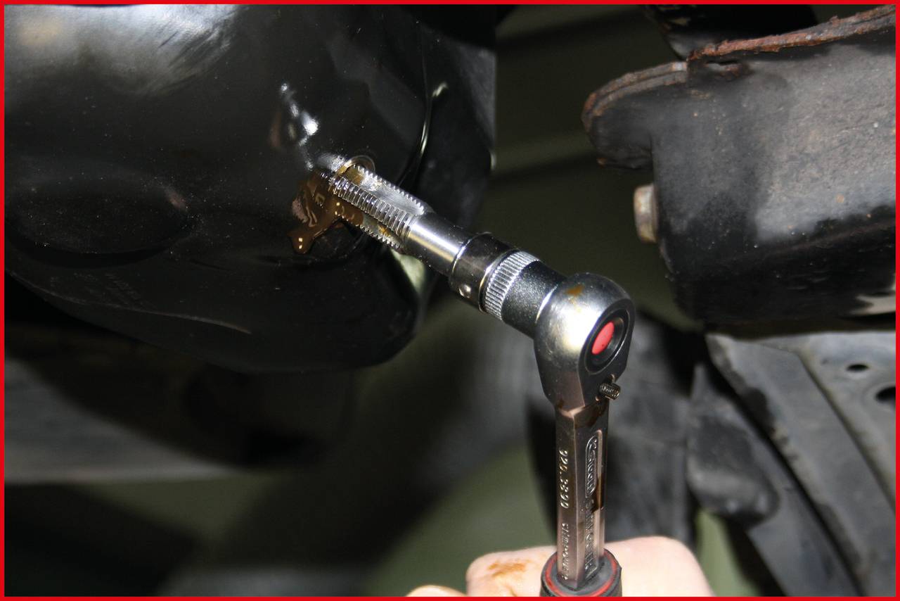 Nahaufnahme einer Ratsche, die einen Schraubenkopf an einem Metallgehäuse dreht. Mechanische Arbeit an einem Fahrzeug.