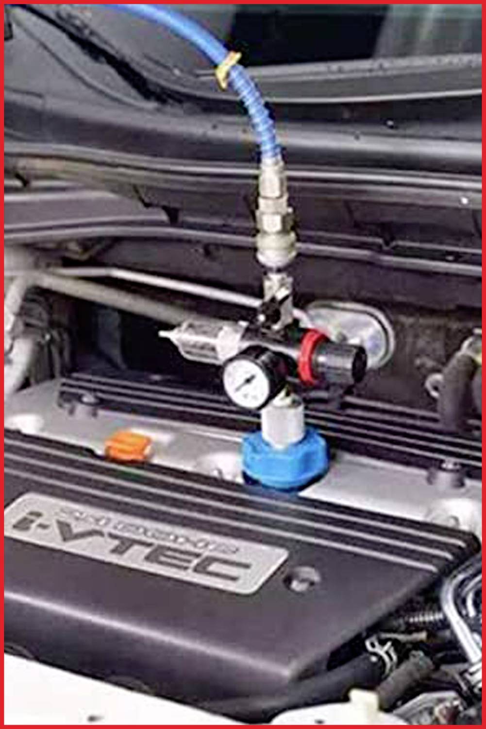 Ein Motorraum mit einem blauen Werkzeug, das an die Motorabdeckung angeschlossen ist. Ein Manometer und Schläuche sind sichtbar.