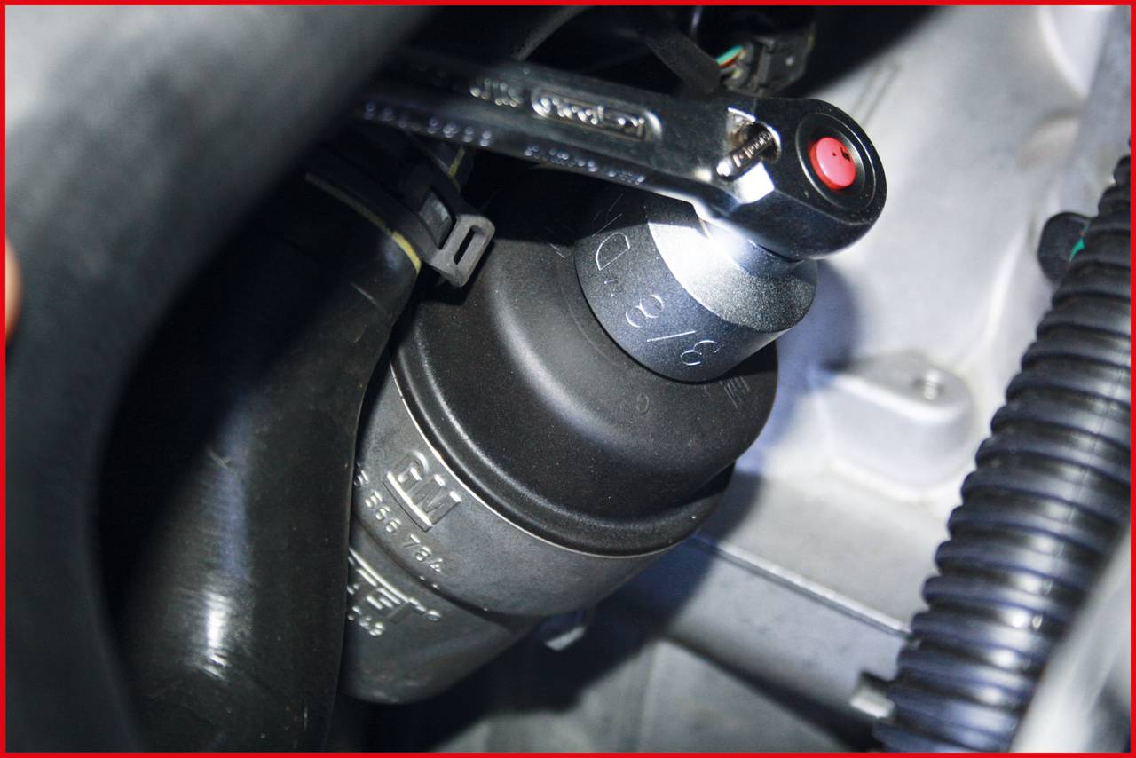 Mechaniker befestigt einen Ölfilter mit einem Schraubenschlüssel im Motorraum eines Autos.