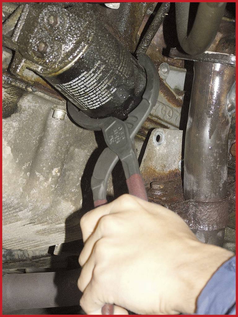 Eine Person verwendet eine Rohrzange, um einen ölverschmierten Auto-Ölfilter in einem Motorraum zu entfernen.