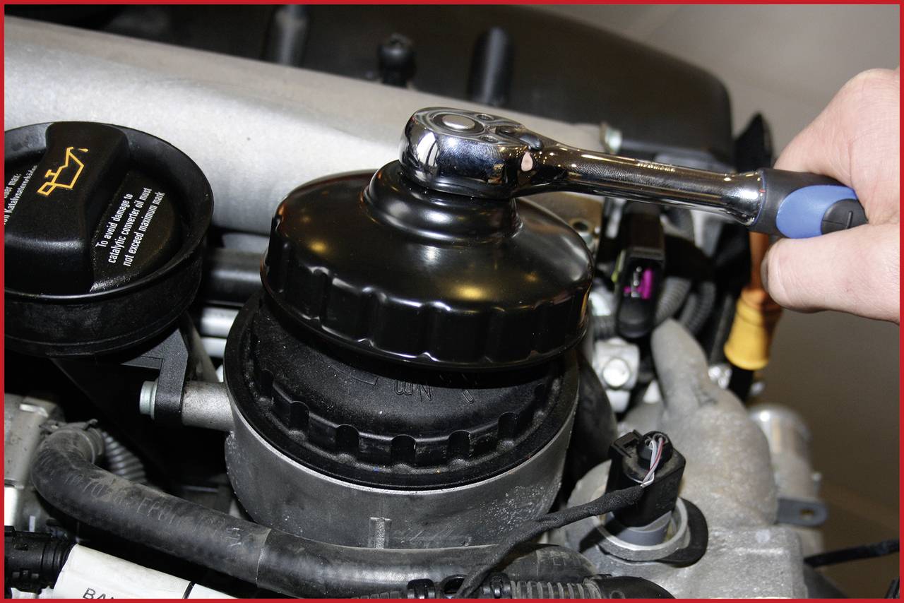Eine Hand nutzt einen Schraubenschlüssel, um einen Ölfilter im Motorraum eines Autos zu wechseln.
