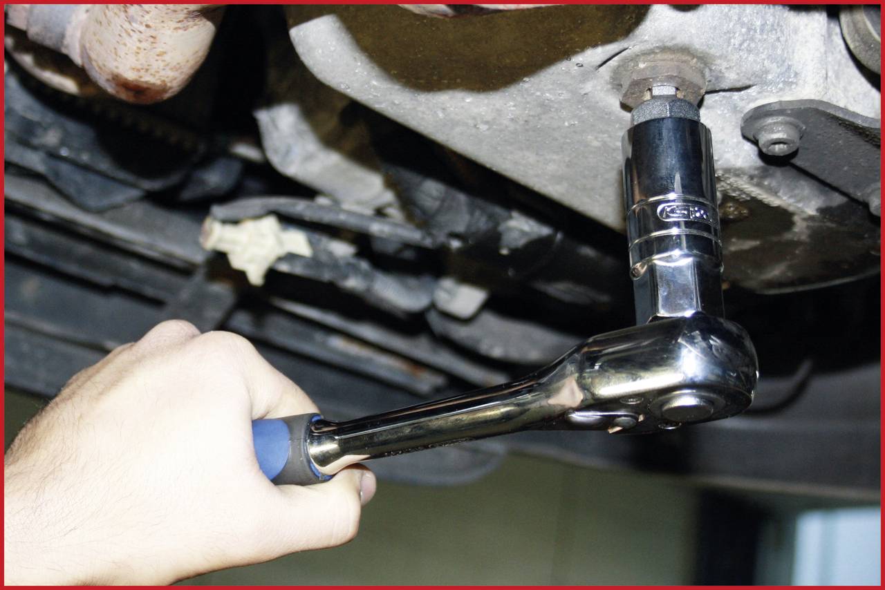 Eine Hand zieht eine Schraube mit einer Ratsche an einem Fahrzeugmotor an.