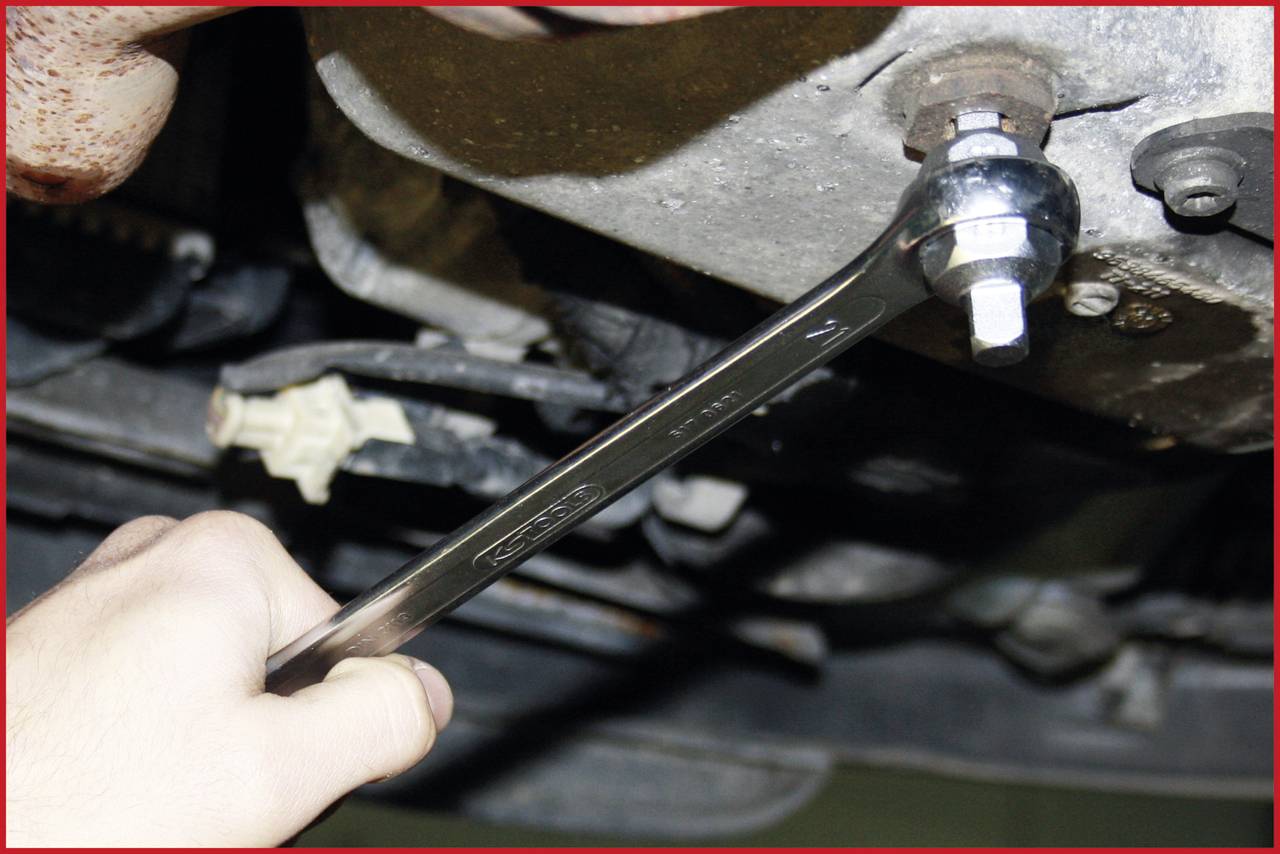 Eine Hand hält einen Schraubenschlüssel und zieht eine Schraube an einem Fahrzeugmotor an.