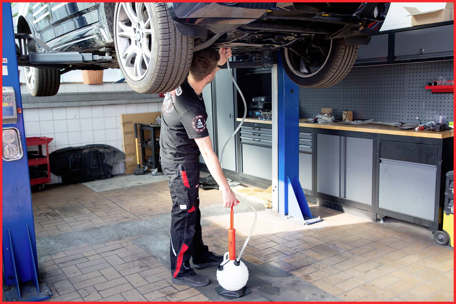 Ein Mechaniker arbeitet in einer Werkstatt an einem Auto, das auf einer Hebebühne steht.