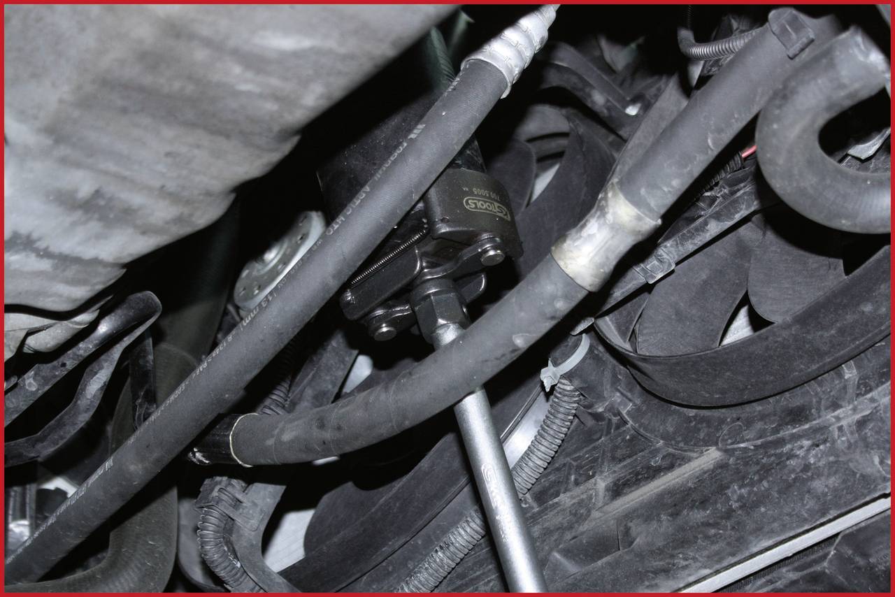 Ein Motorraum mit verschiedenen Schläuchen und Metallteilen. Die Bildmitte zeigt einen schwarzen Zylinder mit einer Rohrverbindung.