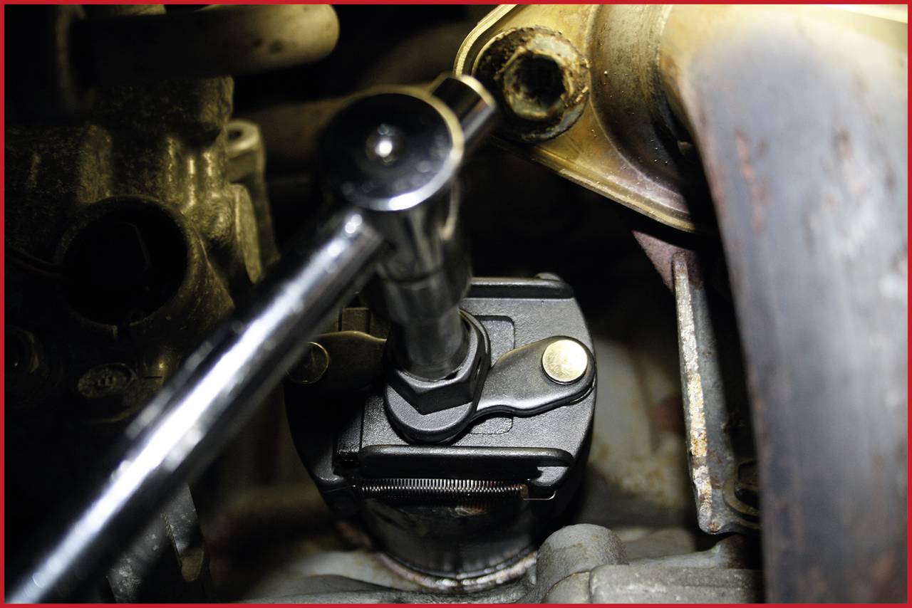 Ein Ratschenwerkzeug zieht eine Schraube im Motorraum an. Es zeigt den engen Arbeitsbereich und die mechanische Präzision.