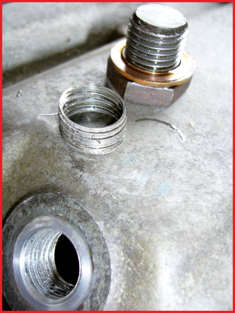 Nahaufnahme eines beschädigten Gewindes in einem Metallblock mit einer Helicoil-Einsatzreparatur und einer gelösten Schraube daneben.