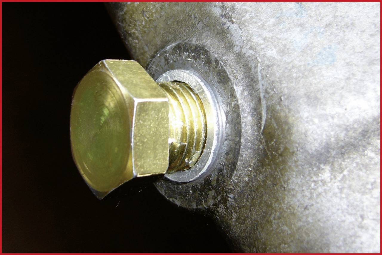 Nahaufnahme einer goldenen Sechskantschraube in eine Metalloberfläche eingeschraubt, zeigt Befestigungstechnik und Materialkontrast.
