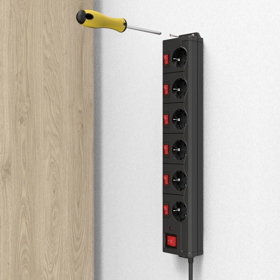 Eine schwarze Steckdosenleiste mit Schaltern ist an einer weißen Wand montiert. Ein Schraubendreher steckt oben in der Leiste.