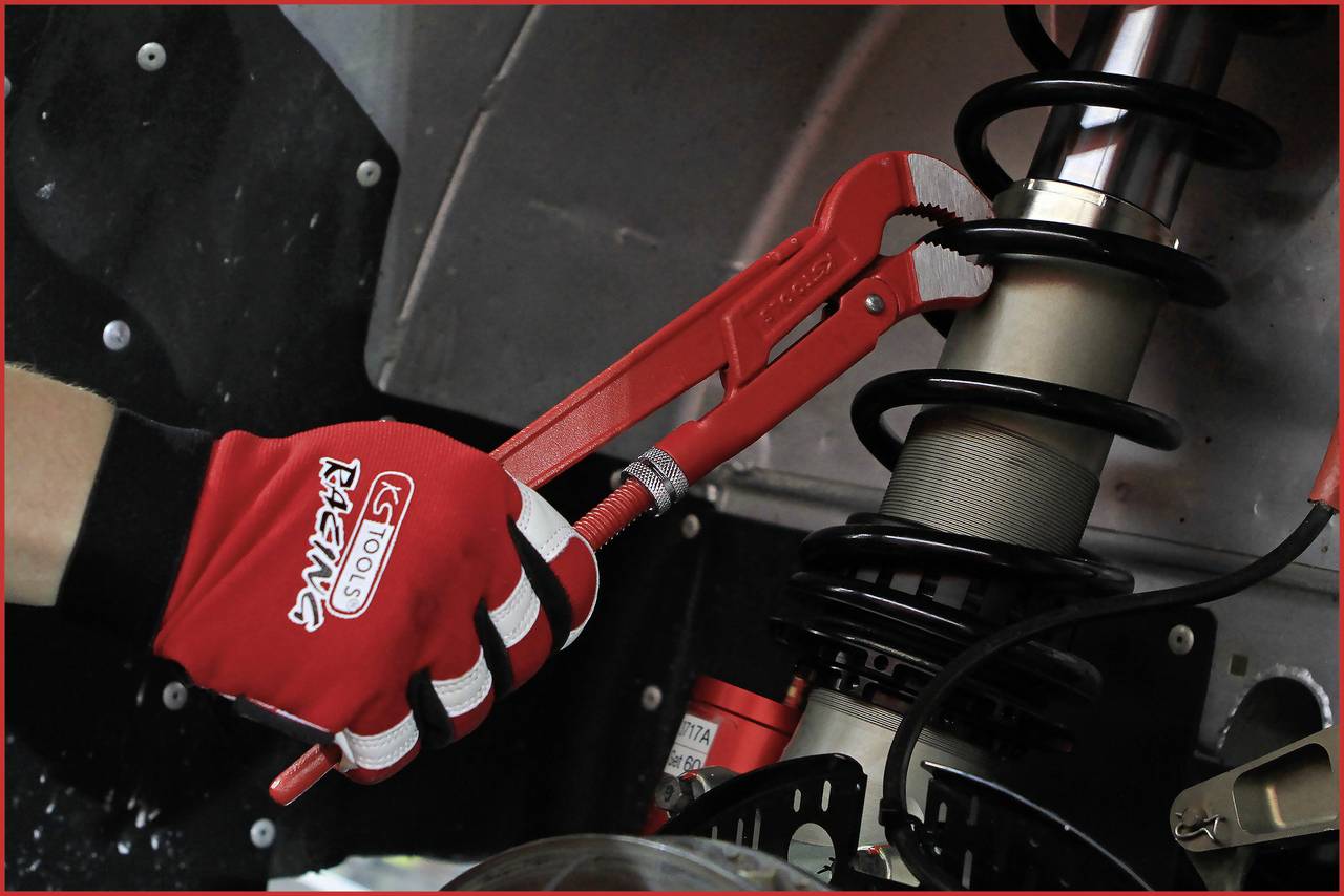 Eine Hand im roten Handschuh hält eine rote Rohrzange und justiert eine Federung.