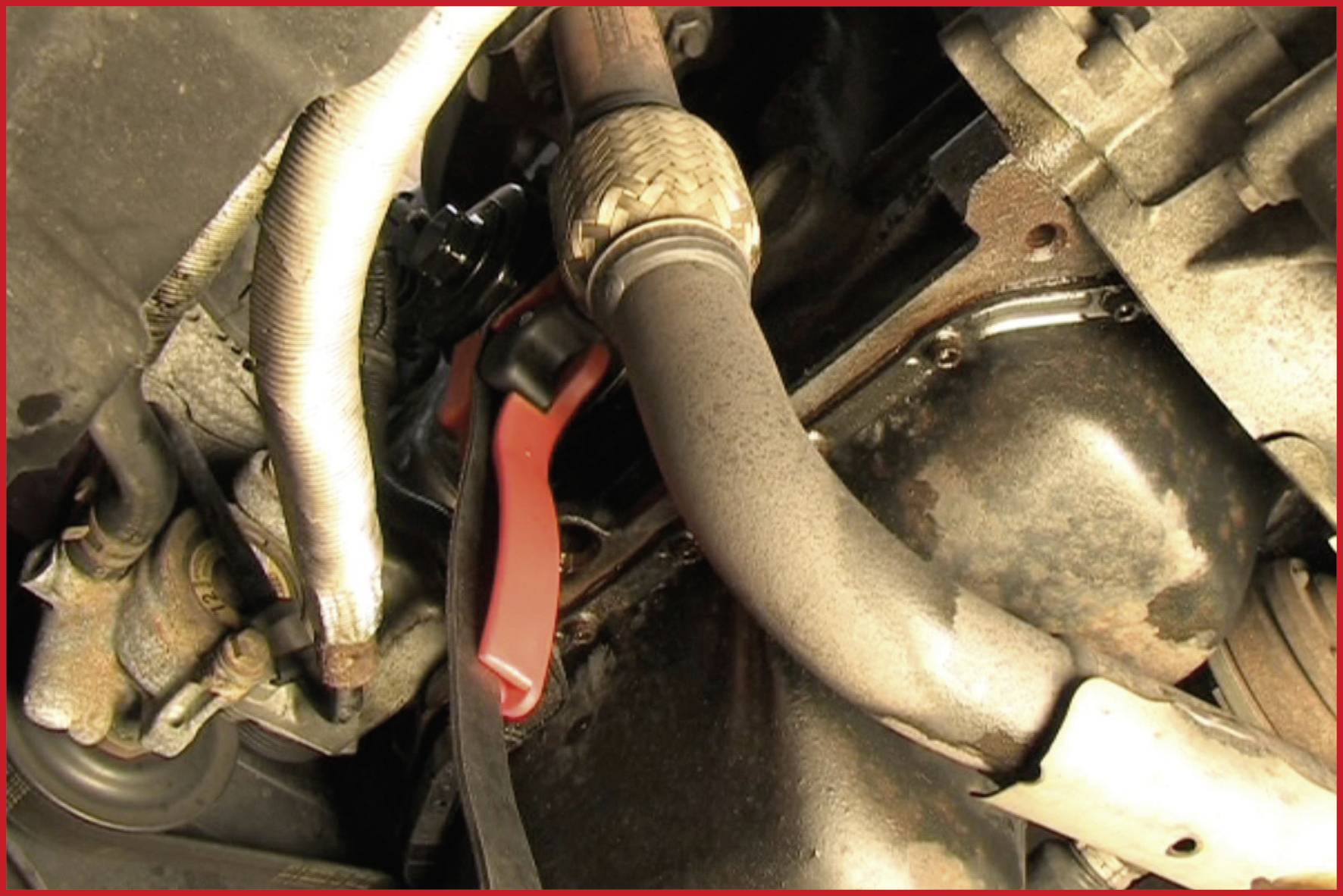 Motormotor mit verschiedenen Schläuchen und Verbindungsstücken in einer Fahrzeugmaschine. Hauptsächlich rostige Teile sichtbar.