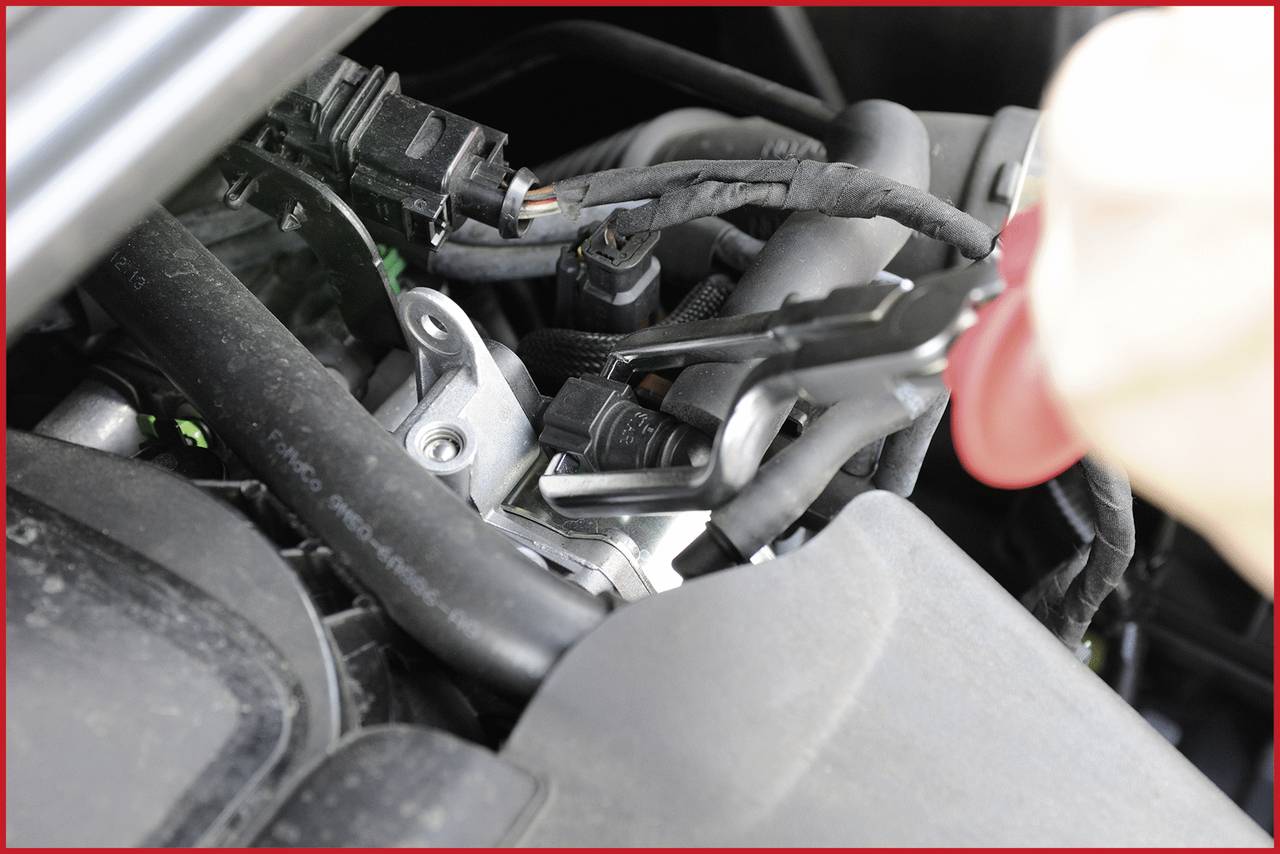 Nahaufnahme eines Automechanikers, der mit einem Werkzeug an einem Motor arbeitet, um Kabel zu reparieren oder zu verbinden.