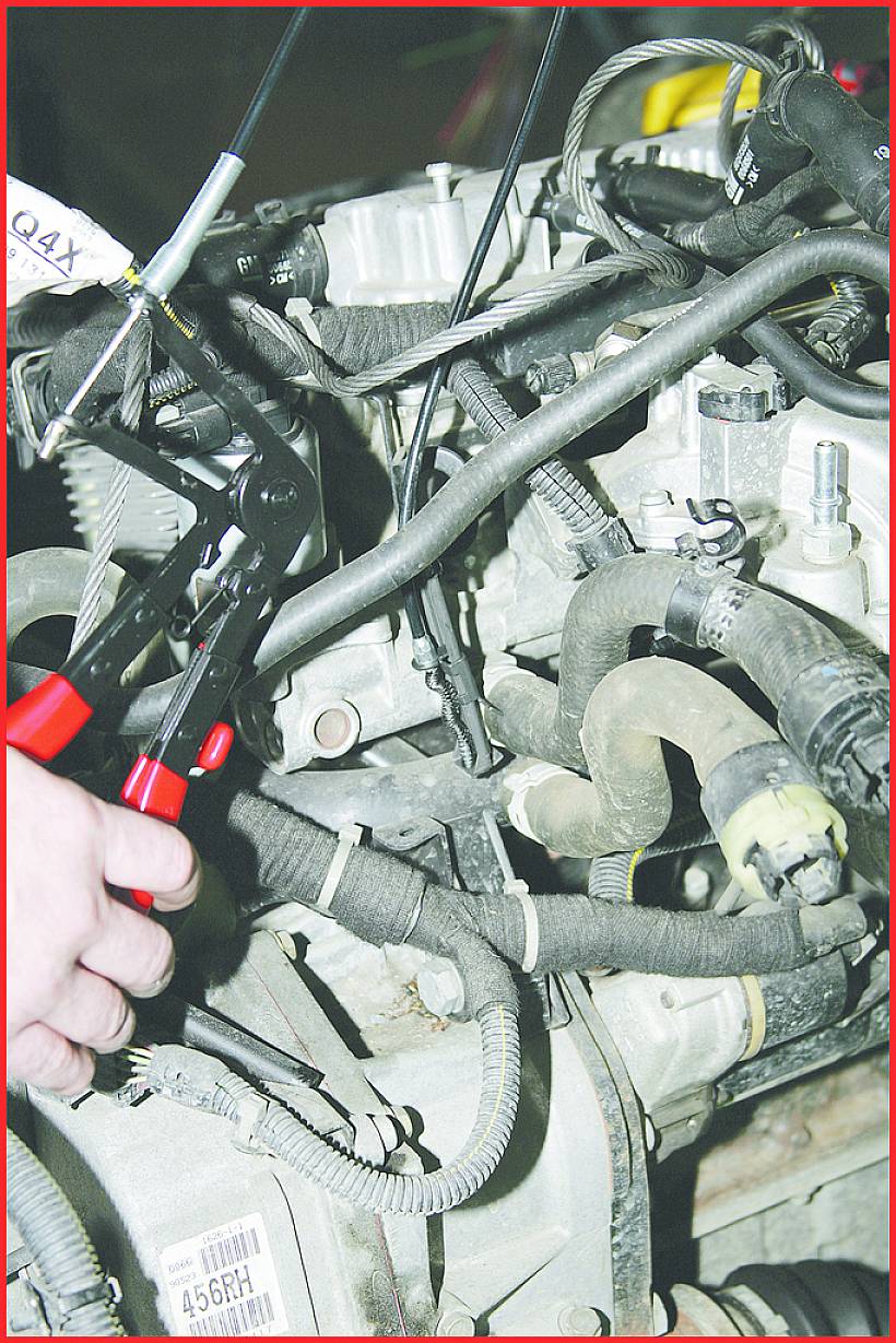 Eine Person verwendet eine Zange, um Kabel an einem Automotor zu reparieren. Verschiedene Schläuche und Drähte sind sichtbar.