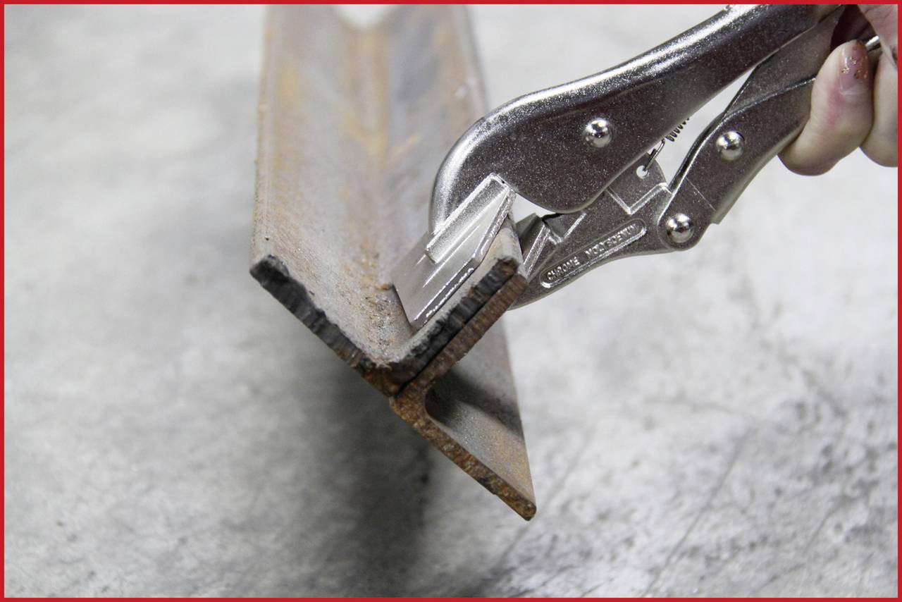 Eine Hand hält eine rostige Metallkante mit einer Zange fest. Die Szene zeigt eine Reparatur- oder Wartungssituation.