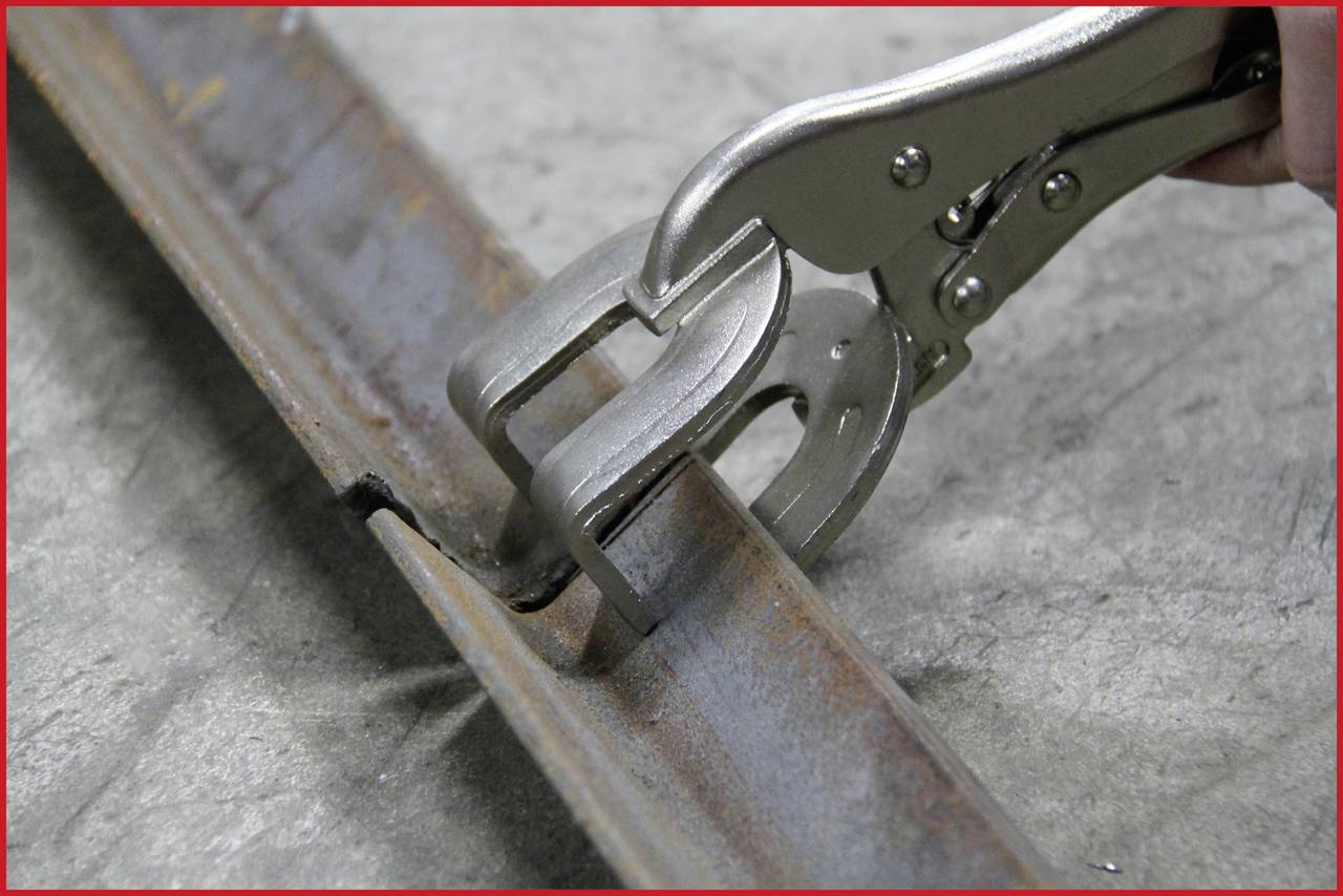 Eine Klemme greift eine Metallkonstruktion, möglicherweise zur Stabilisierung oder Montage. Die Klemme zeigt eine gezackte Greiffläche für festen Halt.