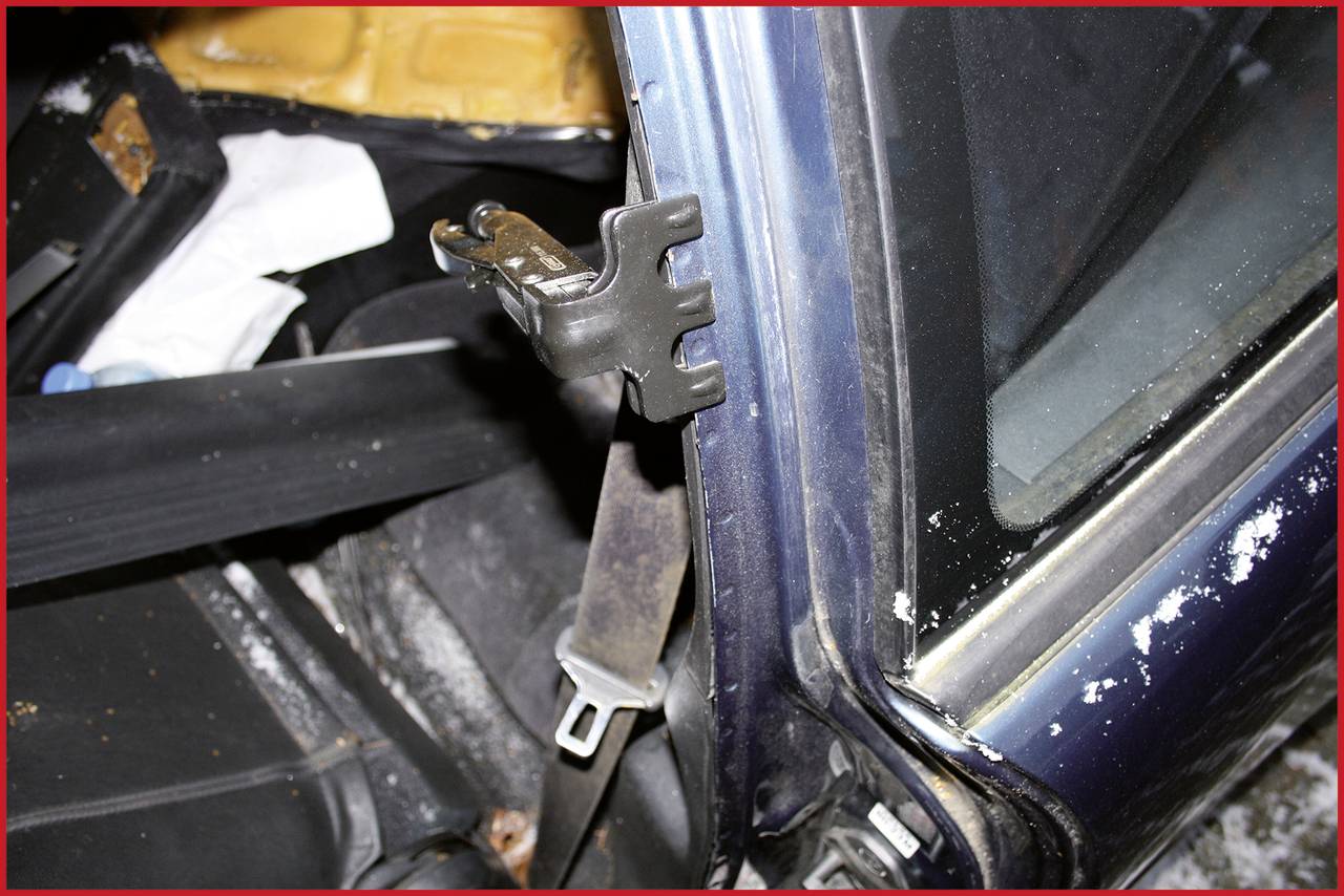 Ein beschädigter Autoinnenraum mit einem abgenutzten Sicherheitsgurt und einer gebrochenen Seitenscheibe.