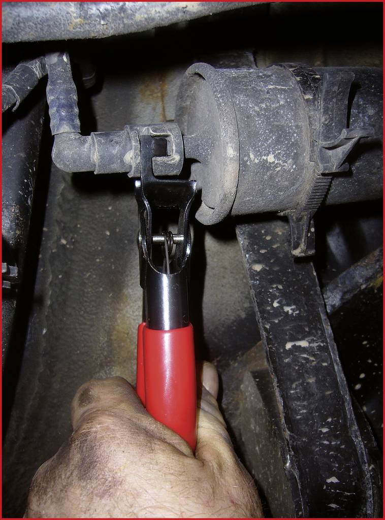 Hand hält eine Zange, um eine enge Verbindung an einem verschmutzten Rohr oder Schlauch in einem Auto zu lösen oder zu reparieren.