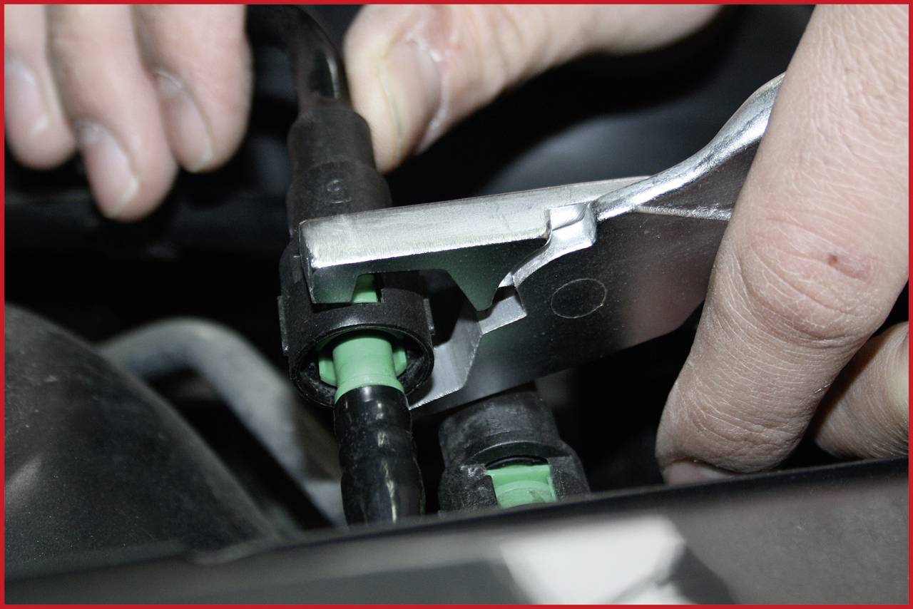 Nahaufnahme einer Hand, die mit einer Zange einen Schlauchanschluss im Auto öffnet.