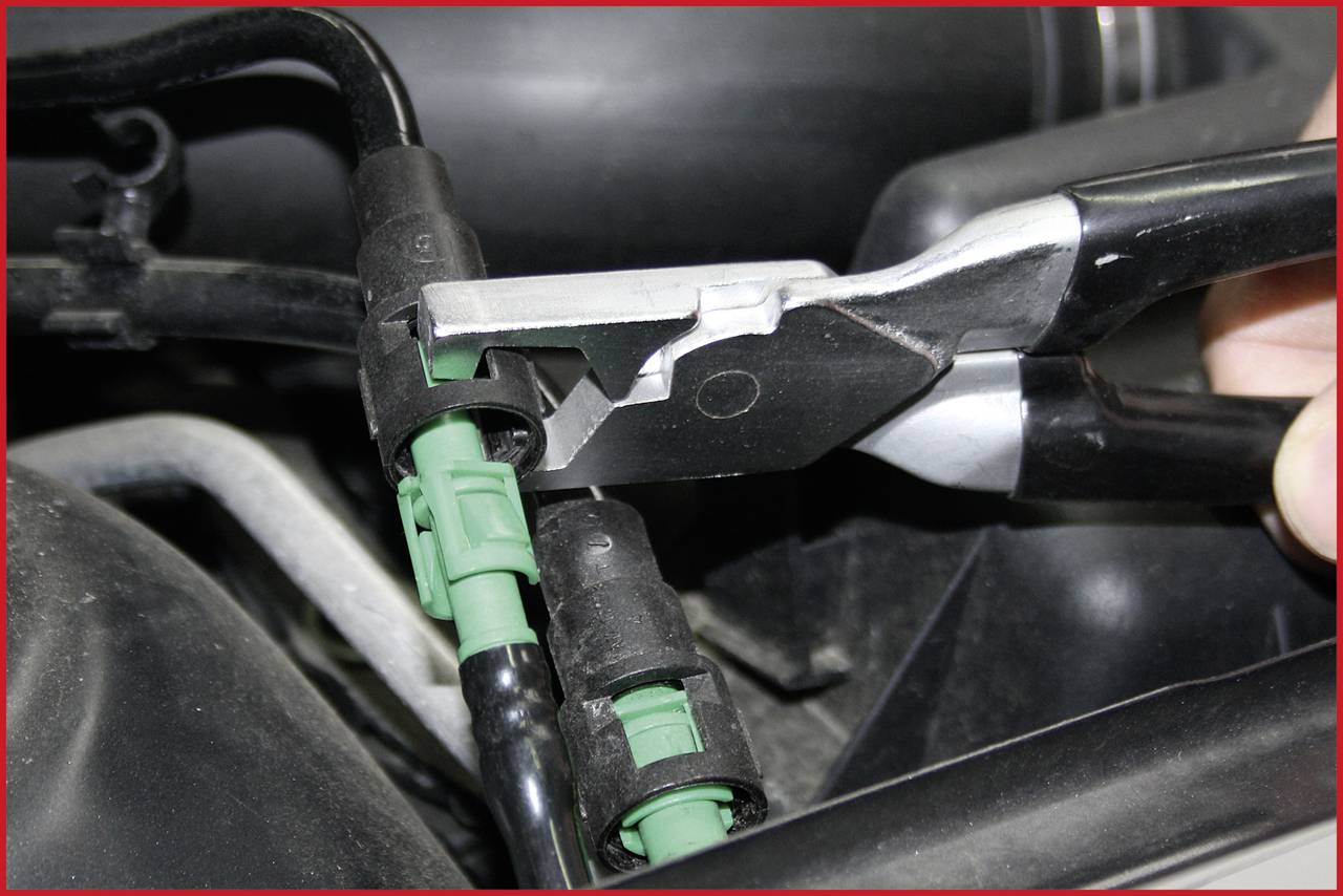 Nahaufnahme eines Werkzeugs, das einen grünen Steckverbinder in einem Motorkomponentenbereich hält, vermutlich zur Reparatur oder Wartung.