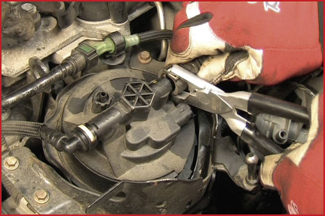 Ein Mechaniker mit roten Handschuhen verwendet eine Zange, um ein Teil in einem Fahrzeugmotor zu reparieren oder einzustellen.