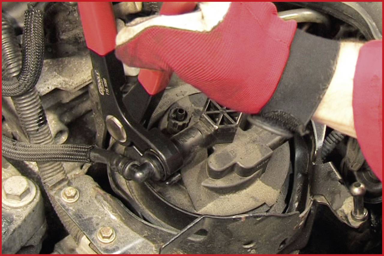 Eine Person mit roten Handschuhen benutzt ein Werkzeug, um eine Schraube in einem Motorraum festzuziehen.
