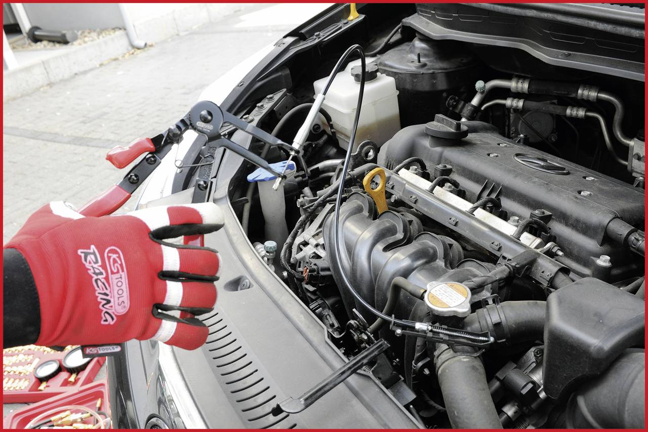 Eine Person mit roten Rennhandschuhen arbeitet an einem geöffneten Auto-Motorraum und benutzt Spezialwerkzeug zur Wartung.