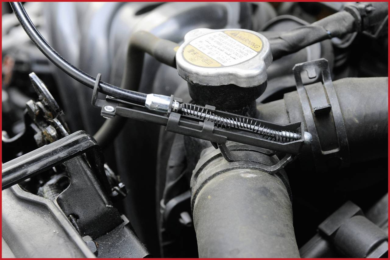 Ein Automotor mit einem offenen Kühlerverschluss. Ein Schlauch mit einer Metallklemme ist sichtbar, umgeben von Metall- und Kunststoffteilen.