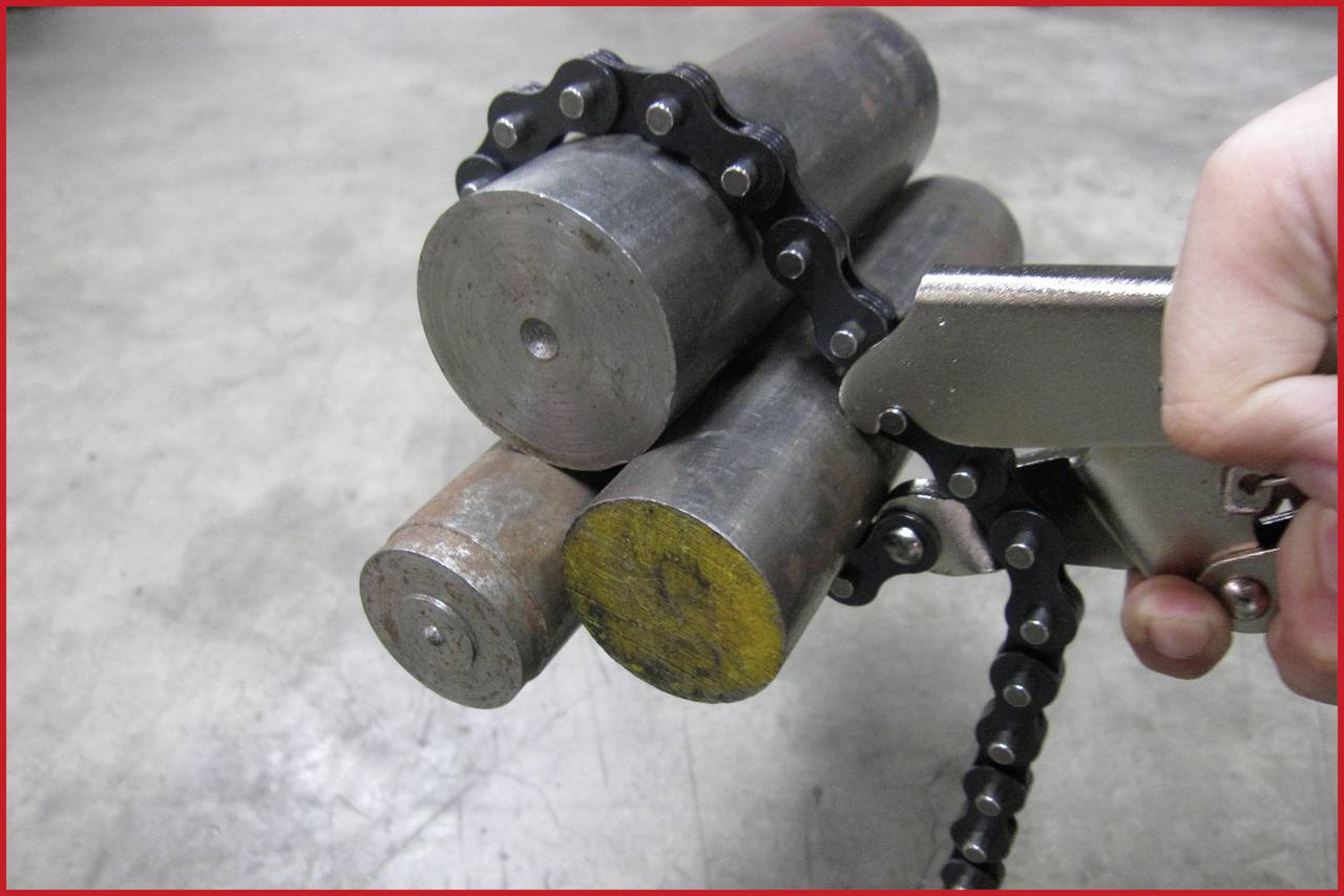 Hand hält eine Kettensäge, die um drei Metallzylinder gelegt ist. Die Zylinder sind auf einer grauen Oberfläche platziert.