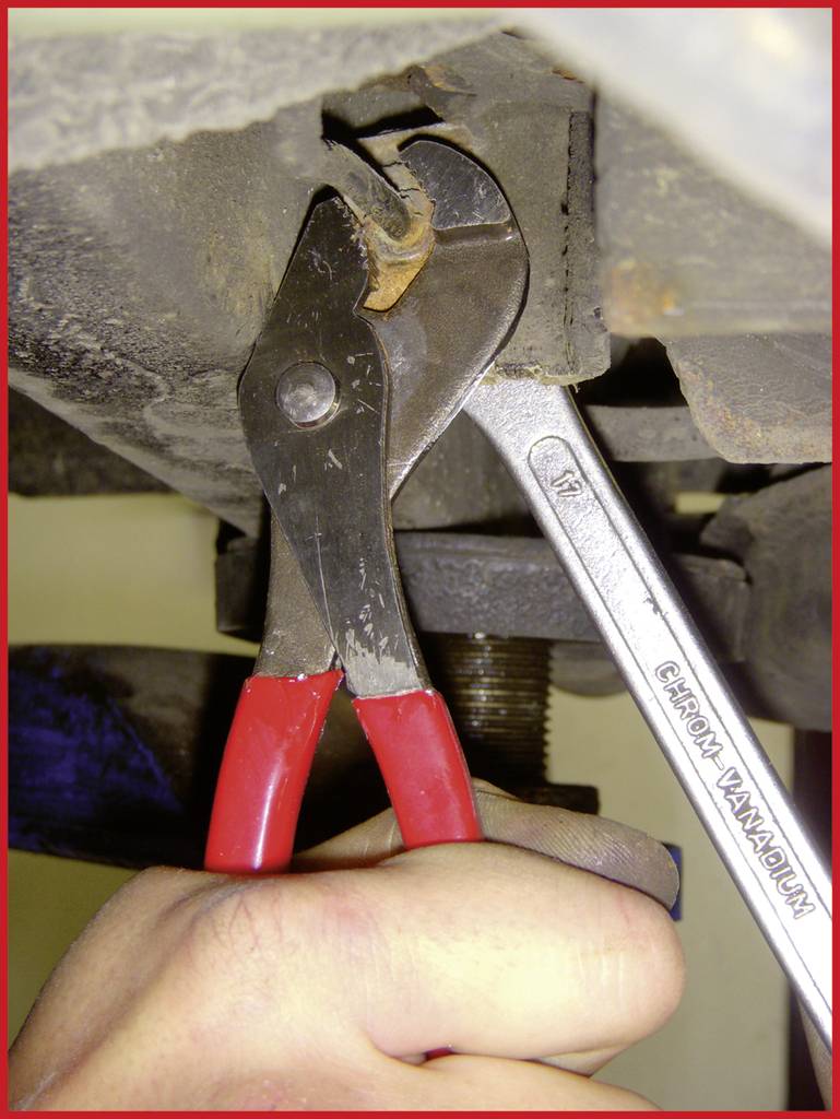 Eine Hand hält eine rote Rohrzange, die ein Metallteil greift, während ein Schraubenschlüssel mit der Aufschrift 'Chrom Vanadium' das Teil fixiert.