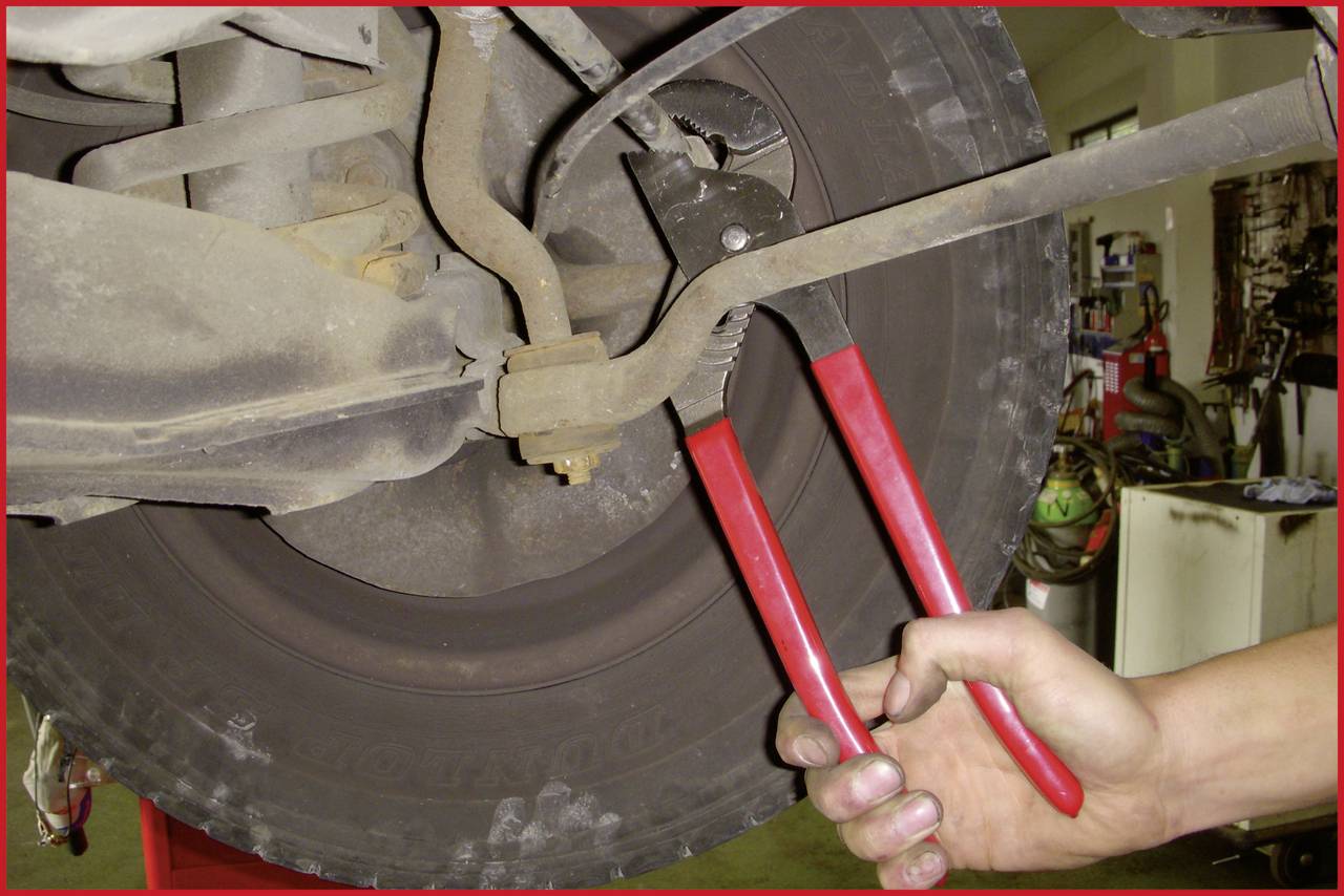 Eine Hand benutzt eine rote Zange, um an einem Fahrzeugrad etwas zu reparieren oder justieren. Der Fokus liegt auf der Arbeit am Autoteil.
