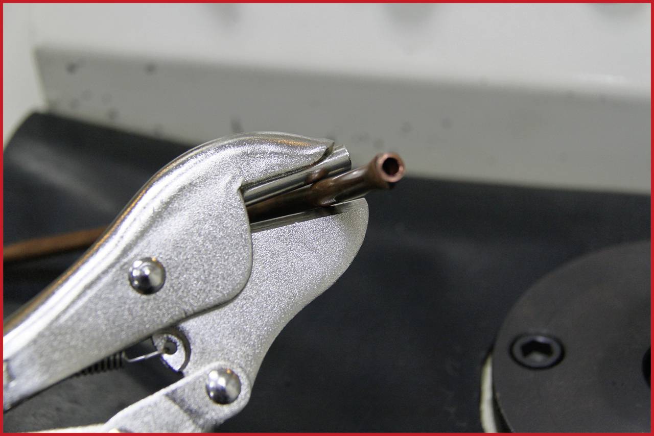 Eine Zange hält ein dünnes Metallrohr auf einer Werkbank. Sie wird wahrscheinlich für Reparatur- oder Installationsarbeiten verwendet.