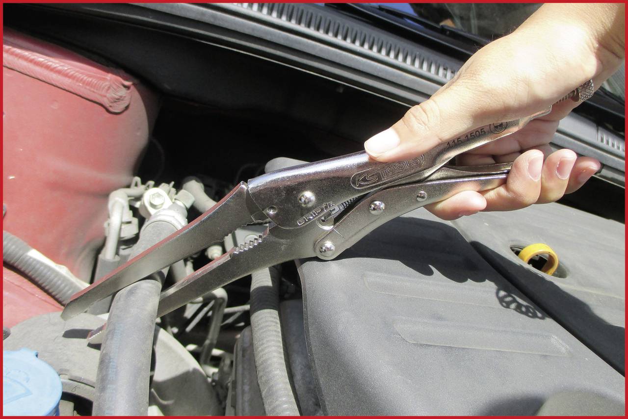 Eine Hand hält eine Greifzange, die einen Schlauch unter der Motorhaube eines Autos festhält.