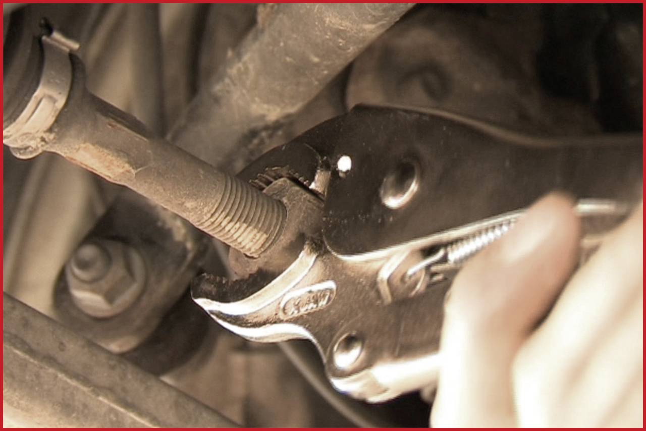 Eine Hand hält eine Rohrzange und zieht eine Mutter an einem Autoteil fest. Das Bild zeigt eine Reparatursituation im Fahrzeug.