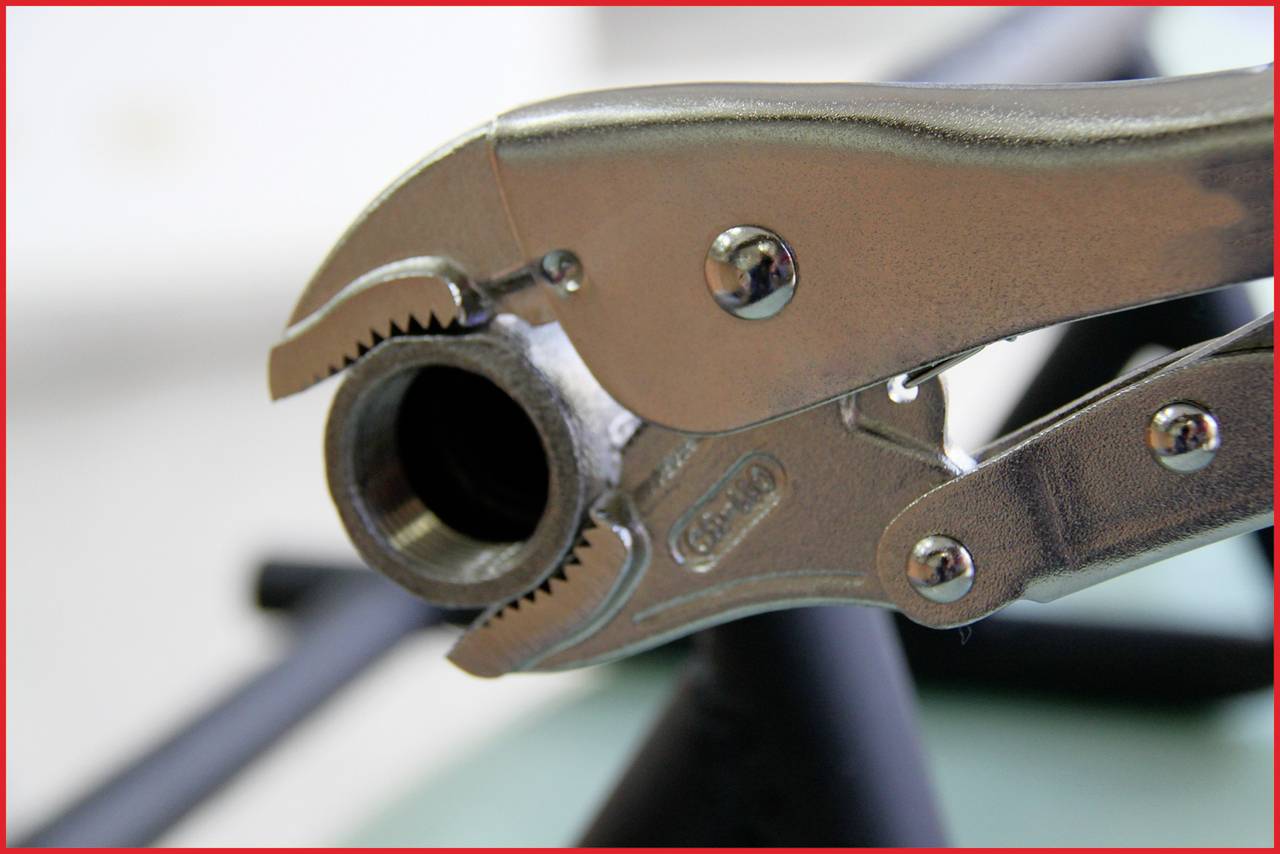 Nahaufnahme einer Metallzange, die ein Rohr greift, in einem Raum mit unscharfem Hintergrund.