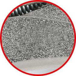 Nahaufnahme eines glitzernden grauen Stoffes mit einer roten Umrandung. Im Hintergrund ist ein Teil einer Metallspule sichtbar.